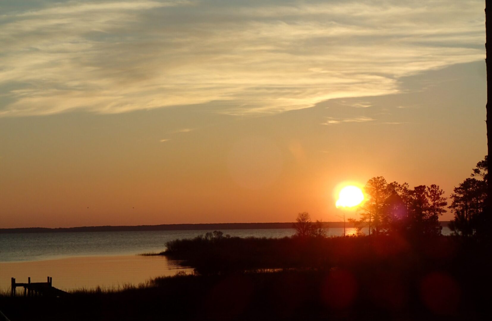 A sunset over the water with trees in front of it.